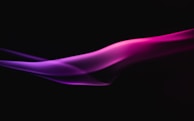 A smooth, flowing wave of vibrant pink and purple light or smoke against a black background, creating a dynamic and ethereal visual effect.