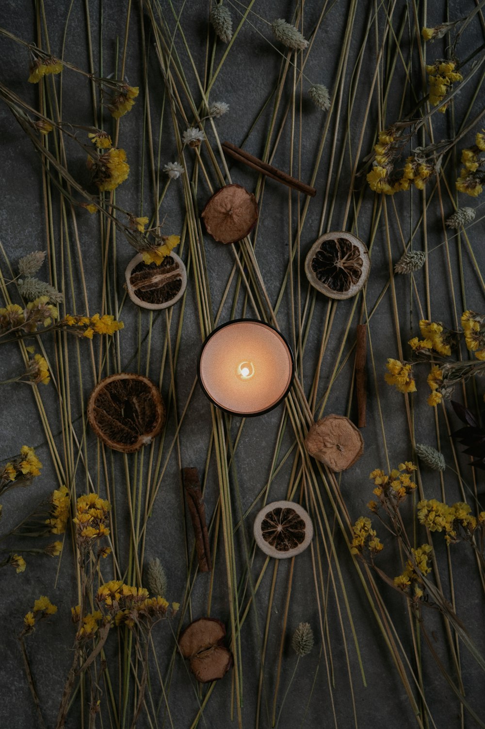 eine brennende Kerze, umgeben von getrockneten Blumen und Zweigen