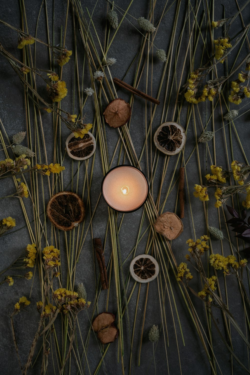 a lit candle surrounded by dried flowers and herbs