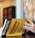 A person with long, wavy hair is holding a book titled 'Mometrix Test Preparation: Secrets Study Guide'. The cover is bright yellow with black text. The background appears blurred, focusing on the book.
