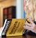 A person with long, wavy hair is holding a book titled 'Mometrix Test Preparation: Secrets Study Guide'. The cover is bright yellow with black text. The background appears blurred, focusing on the book.