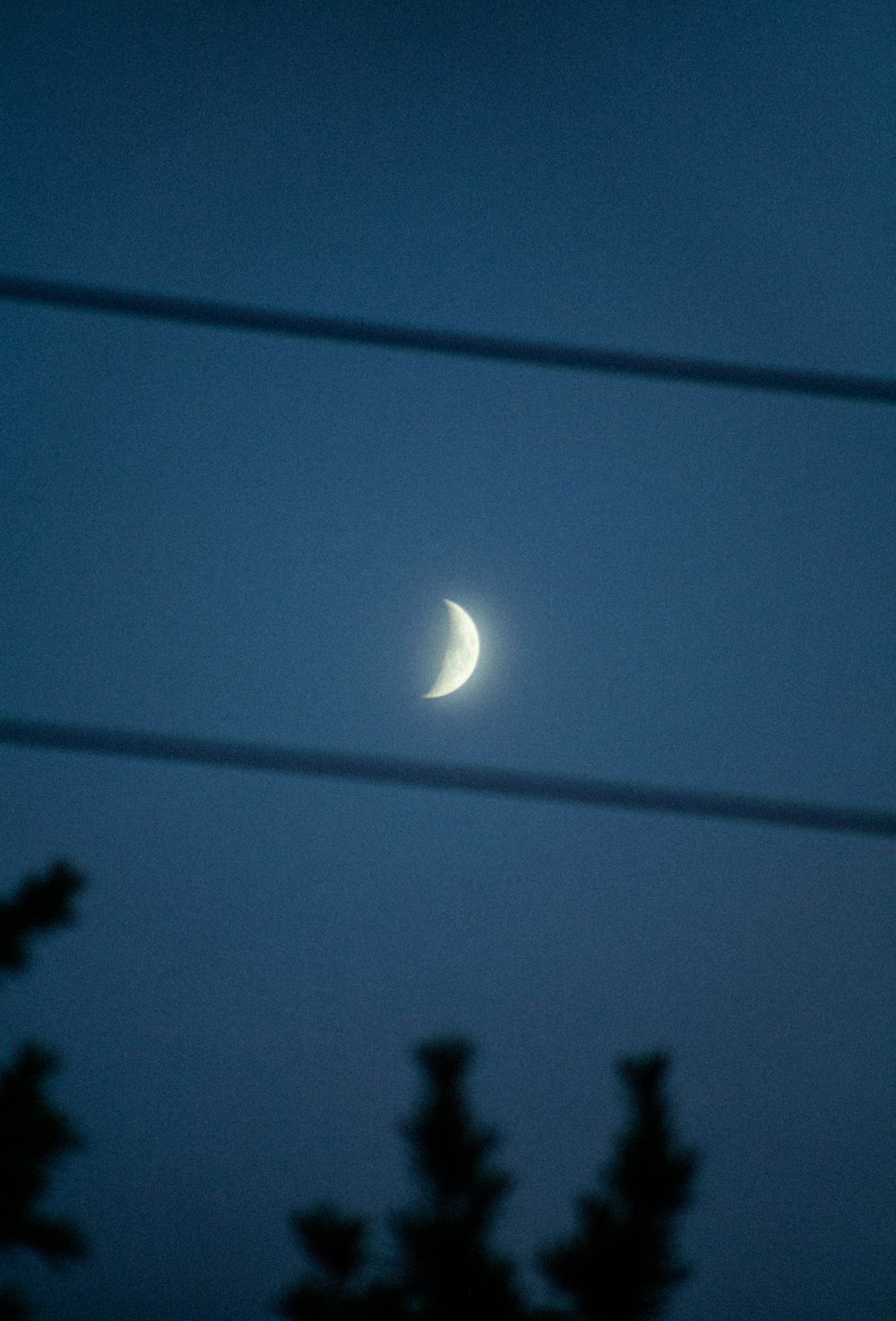 a half moon seen through power lines at night