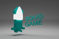 A stylized 3D squid-shaped object with turquoise and white colors. The text 'SQUID GAME' is displayed next to the object in the same turquoise color. The background is a gradient of dark to light gray.