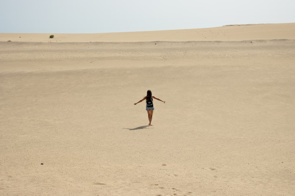 a woman walking across a sandy field with her arms outstretched