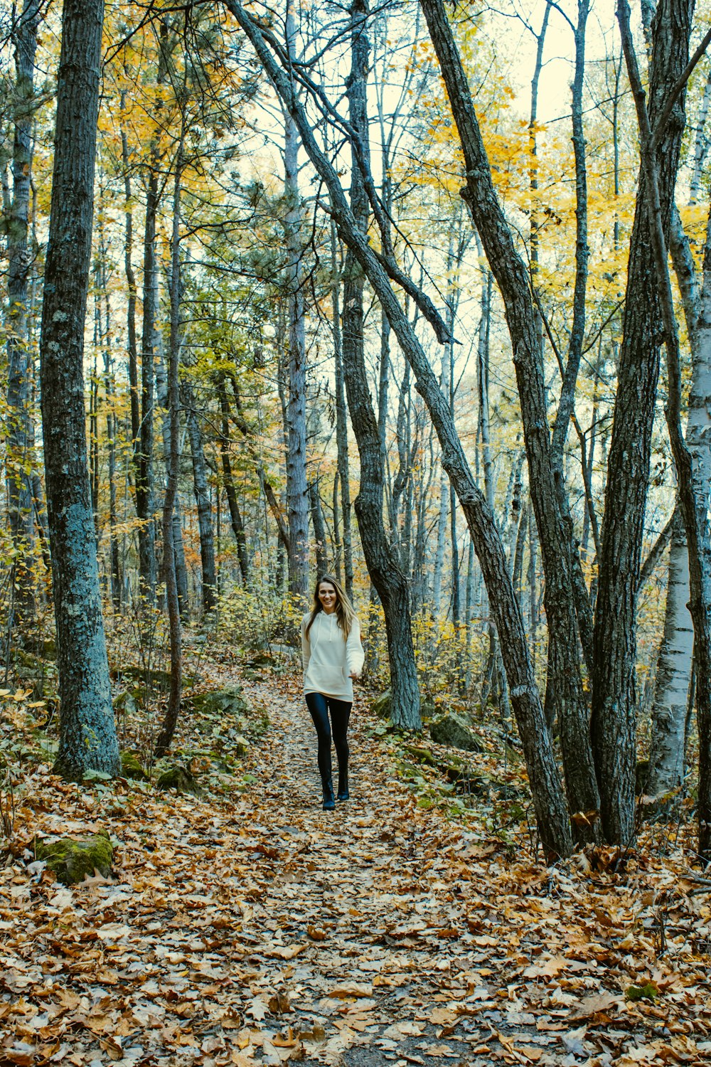 a woman walking down a leaf covered path in the woods