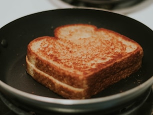 A grilled cheese in a frying pan almost done.