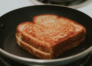 A grilled cheese in a frying pan almost done.