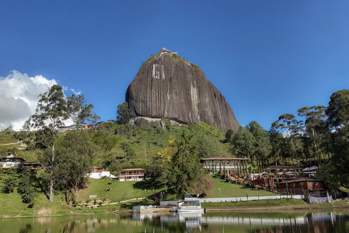 A large granite rock formation rising above a lush green hillside in the Guatape region of Colombia showing the monolithic El Penon de Guatape