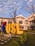 A large sign with the letters 'USL' stands prominently in a landscaped area with green grass and plants. The building behind the sign is an older architectural style with white and red details. The sky is blue with scattered clouds, and there is a leafless tree in the foreground.