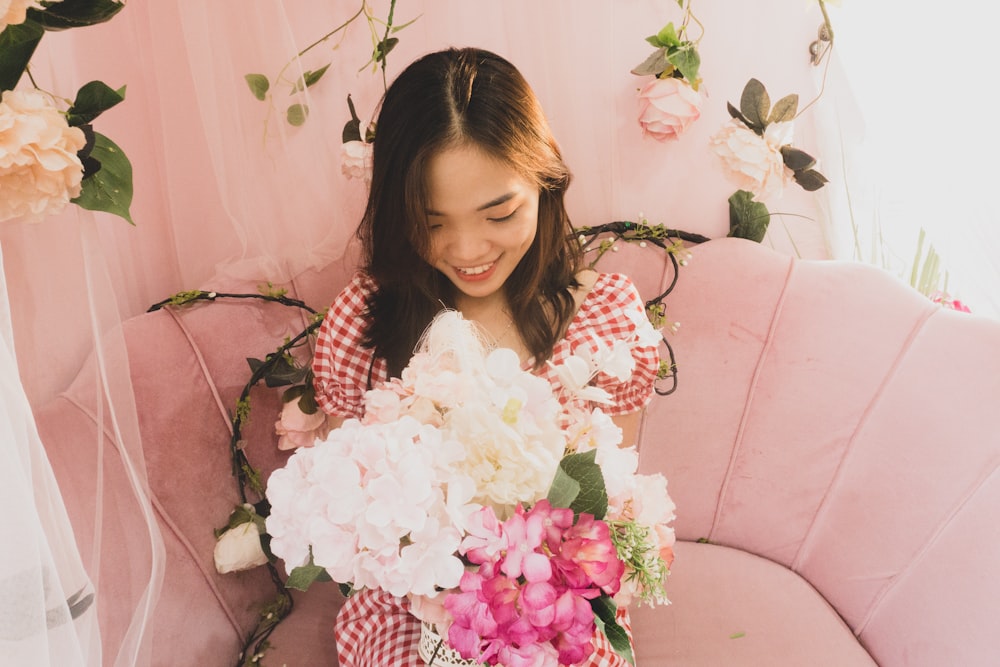 a woman sitting on a pink couch holding a bouquet of flowers