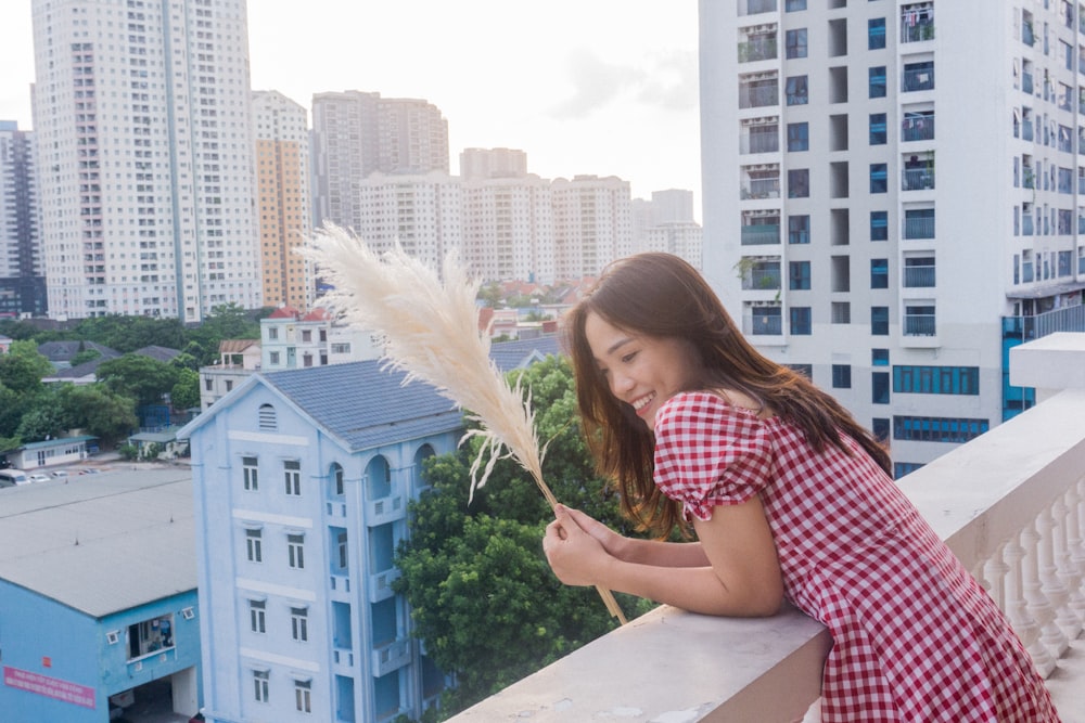 a girl in a red and white checkered dress leaning on a balcony