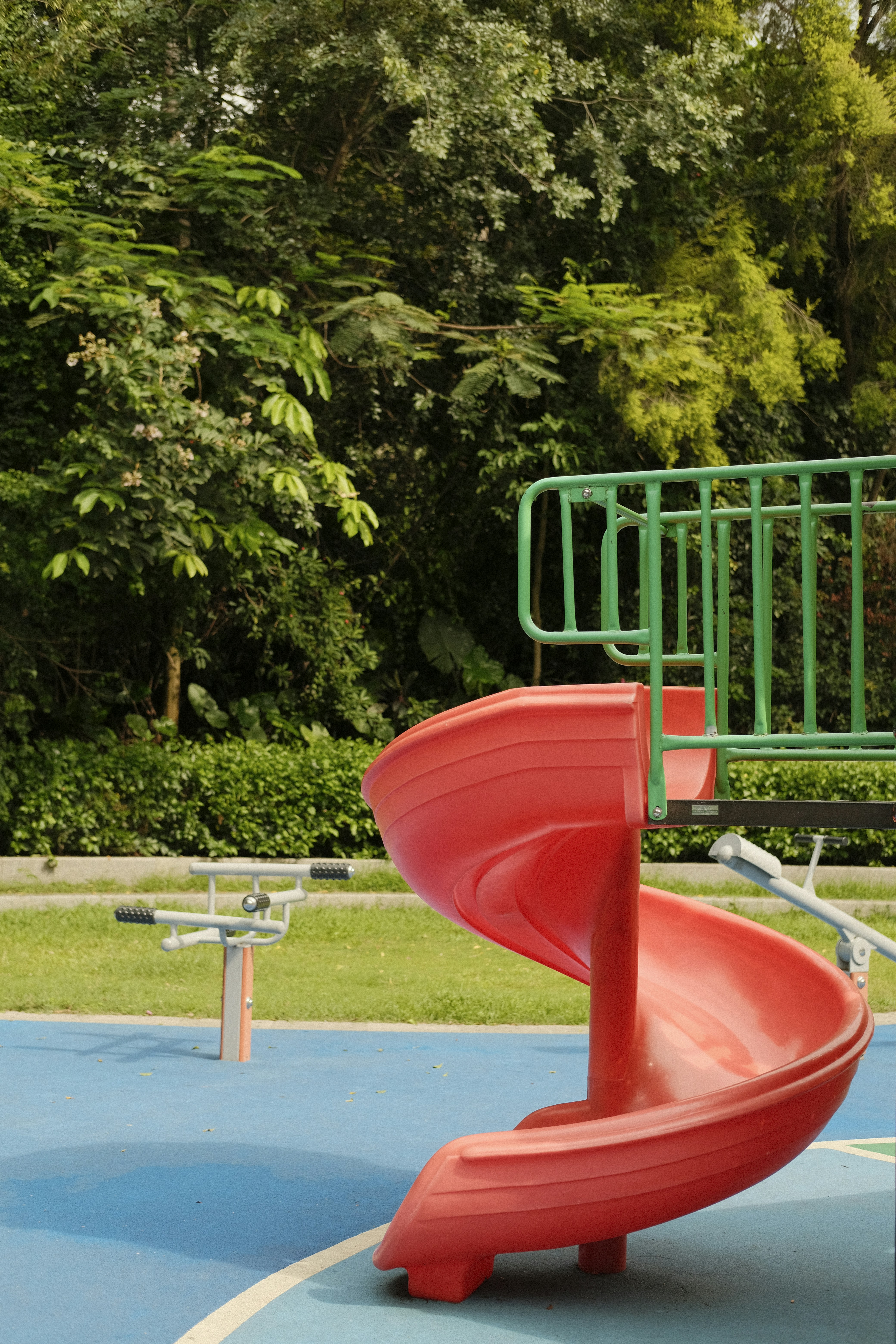a playground with a red slide and green trees in the background