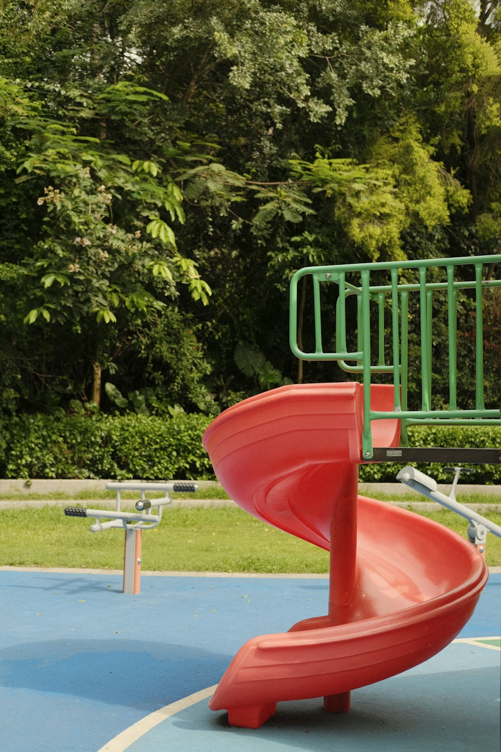 a playground with a red slide and green trees in the background