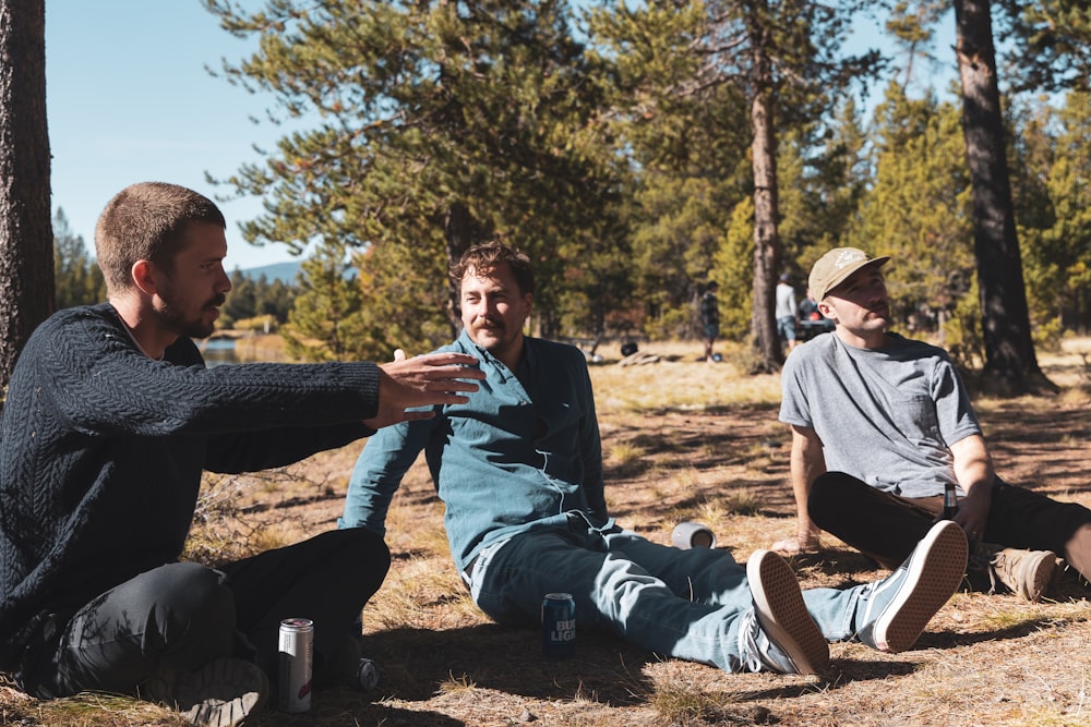 three men sitting on the ground in the woods