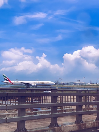 A wide shot of a colorful Emirates Boeing 777 taking off against a clear blue sky at Munich Airport.