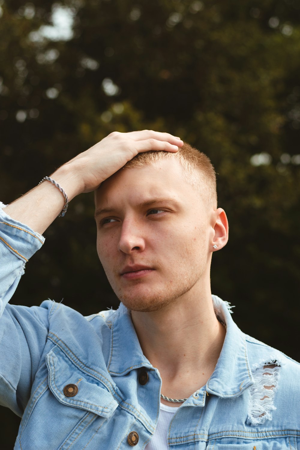 a man in a denim jacket is holding his hand on his head