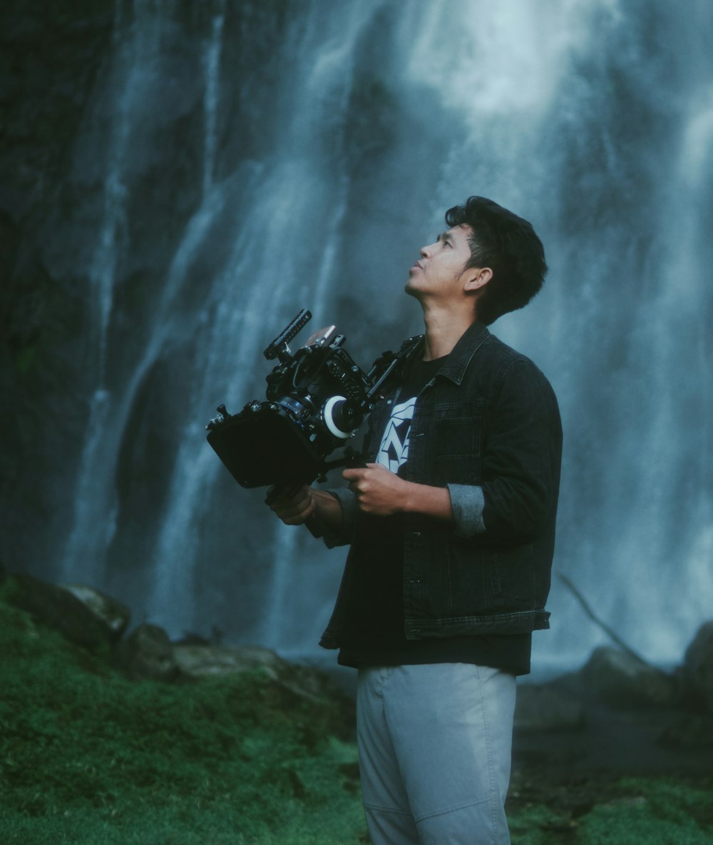 a man holding a camera in front of a waterfall