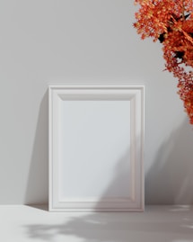a white picture frame sitting next to a vase of flowers