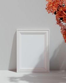a white picture frame sitting next to a vase of flowers