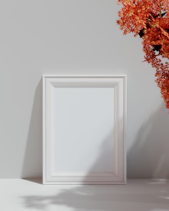 a white picture frame sitting next to a vase of flowers