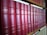 A row of classic books with red leather covers and gold lettering is neatly organized on a wooden bookshelf. The titles and authors' names appear embossed on the spines, suggesting a collection of literary works.