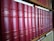 A row of classic books with red leather covers and gold lettering is neatly organized on a wooden bookshelf. The titles and authors' names appear embossed on the spines, suggesting a collection of literary works.