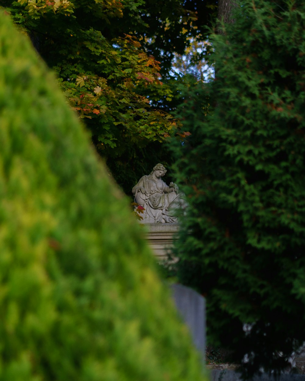 a statue of a man sitting in a park surrounded by trees