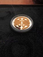 An incense coil is burning in a decorative pattern placed in a small, round container. The surrounding surface is dark, creating a contrast with the light-colored incense ash and the smoke rising gently.