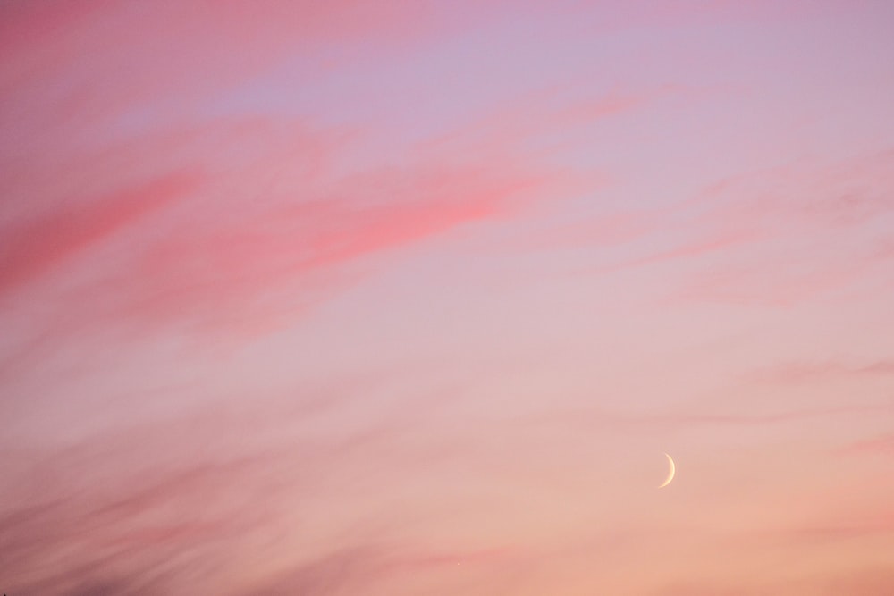 a pink sky with a half moon in the distance