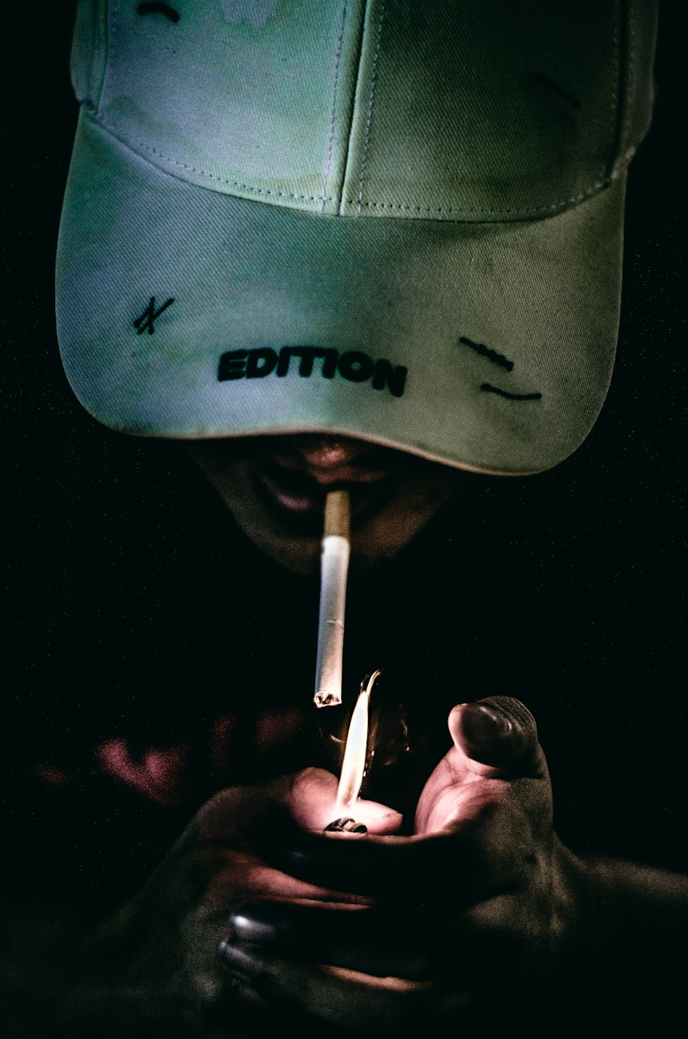 Eine Person, die sich eine Zigarette mit einem Hut auf dem Kopf anzündet