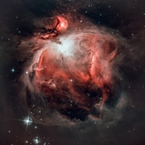 Swirling clouds of gas and dust create a dramatic nebula in space, highlighted by shades of red and white. Stars are scattered throughout the scene, adding brightness and scale to the vast cosmic landscape.