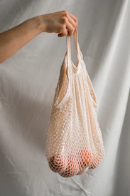 a person holding a mesh bag with a bunch of oranges in it