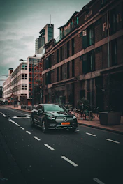 A sleek black Mercedes S-Class parked in front of a modern Amsterdam office building at dusk.