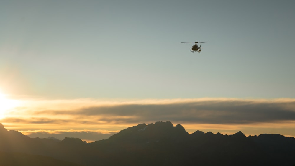 a helicopter flying over a mountain range at sunset