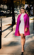 A confident woman in a pastel dress walking through a sunlit urban street.