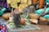 A group of people are seated on the ground, surrounding a ceremonial arrangement that includes traditional gourds, leaves, seeds, and a woven mat. The setting appears to be outdoors, with the participants dressed in colorful garments.