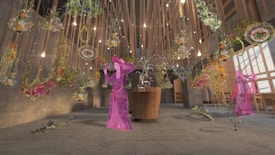 A room with a modern, artistic design featuring suspended floral arrangements and soft lighting. The ceiling is adorned with numerous lightbulbs and natural wood accents. In the center, a wooden table holds a delicate sculpture. Two figures are artistically overlaid, depicted in traditional, vibrant attire and partially transparent.