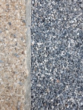 A clear distinction between two types of aggregates is visible. On the left, there are small, beige-colored pebbles mixed with concrete, creating a smooth surface. On the right, larger, gray stones are laid together, forming a textured and rough surface.