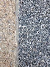 A clear distinction between two types of aggregates is visible. On the left, there are small, beige-colored pebbles mixed with concrete, creating a smooth surface. On the right, larger, gray stones are laid together, forming a textured and rough surface.