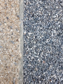 A clear distinction between two types of aggregates is visible. On the left, there are small, beige-colored pebbles mixed with concrete, creating a smooth surface. On the right, larger, gray stones are laid together, forming a textured and rough surface.