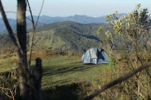 A lightweight camping tent pitched on a grassy hill under a clear blue sky