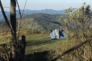 Compact tent pitched on a grassy hill under a clear blue sky