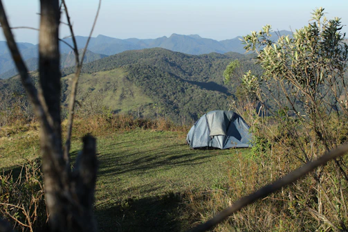 A lightweight camping tent pitched on a grassy hill under a clear blue sky