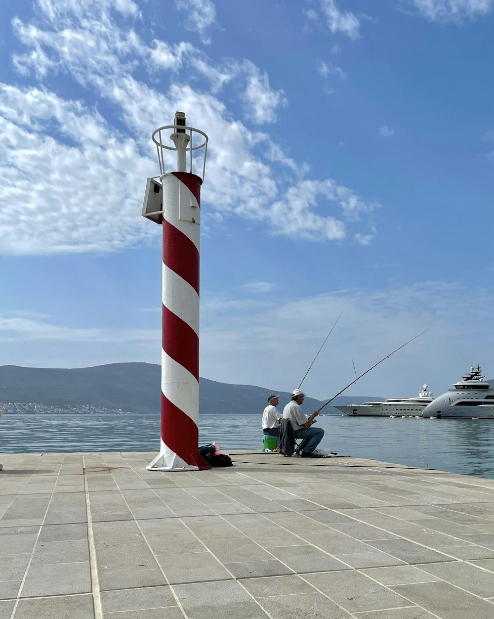 a couple of men sitting on top of a pier next to a light house