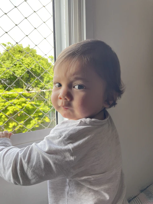 Child playing safely behind a window protected by a sturdy safety net