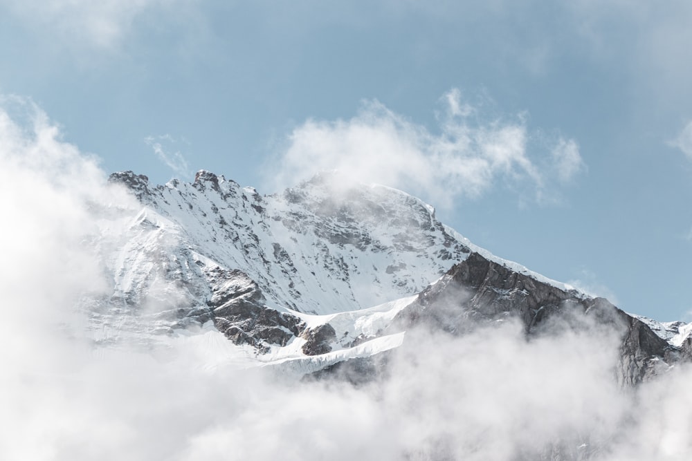 a mountain covered in snow and clouds under a blue sky