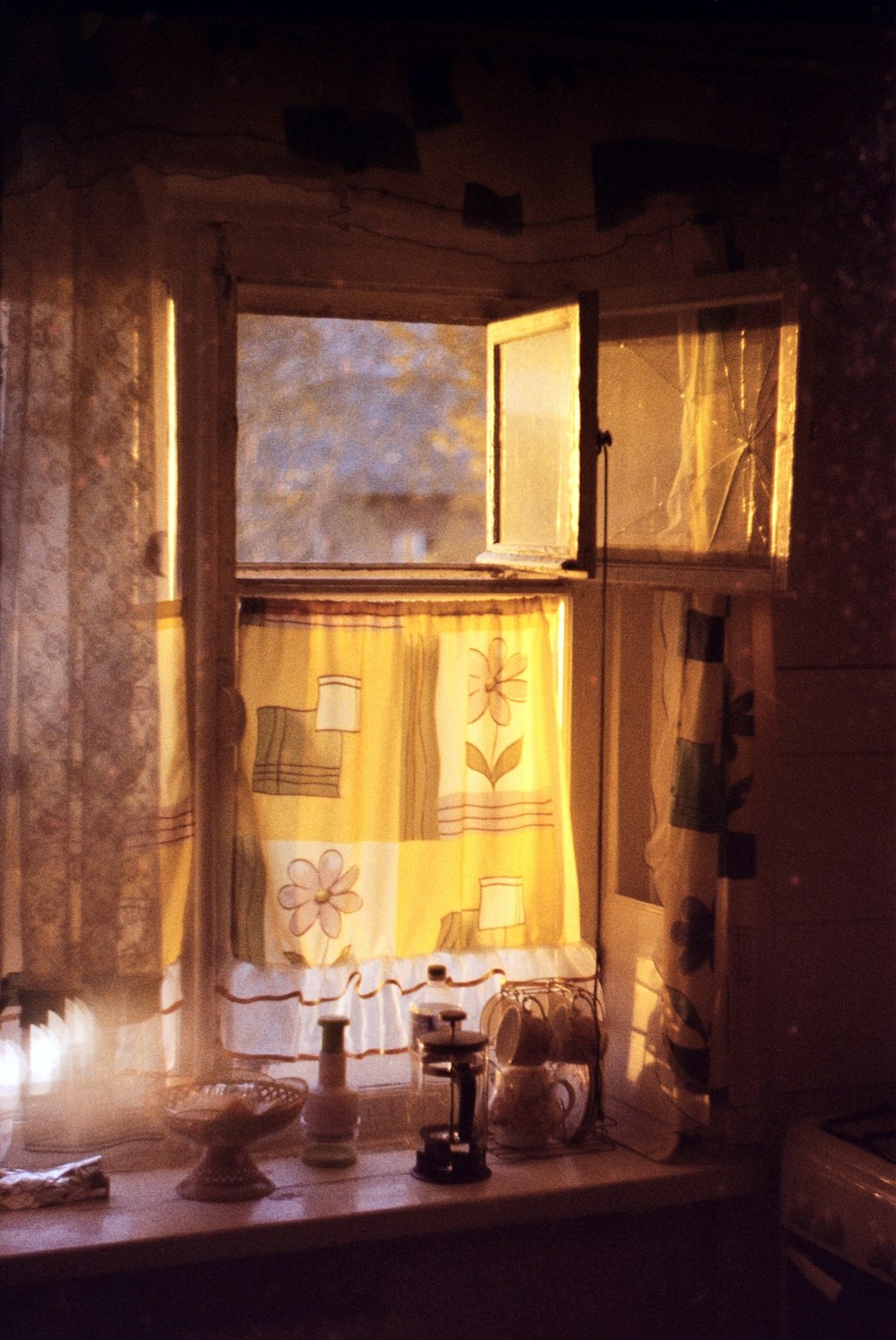 a kitchen window with yellow curtains and dishes on the counter