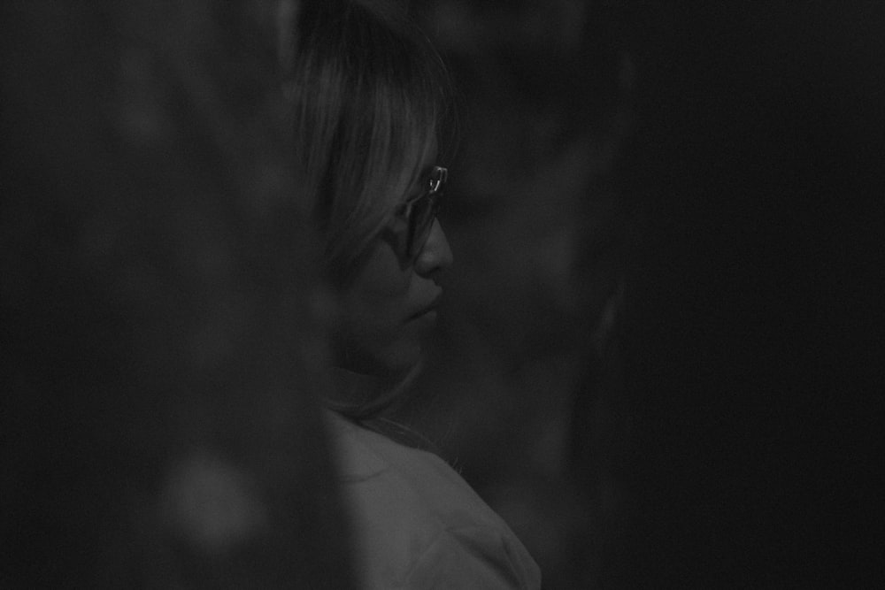 a woman with glasses looking at something in the dark