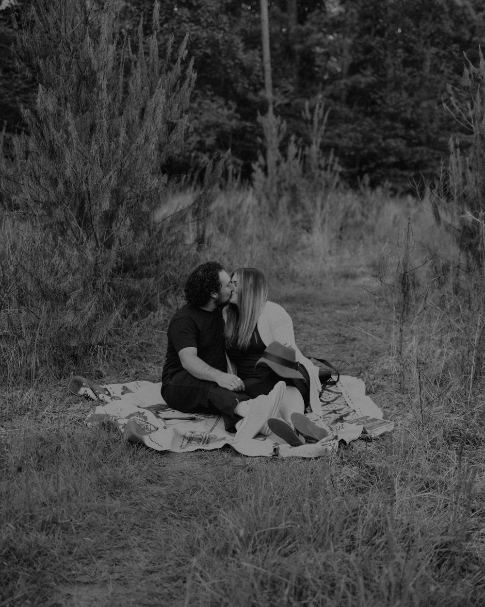 a black and white photo of a couple kissing on a blanket