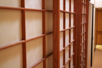 A series of traditional Japanese sliding doors, known as shoji, featuring a wooden grid pattern with translucent paper inserts. The doors are aligned in a hallway, creating a minimalist and serene atmosphere.